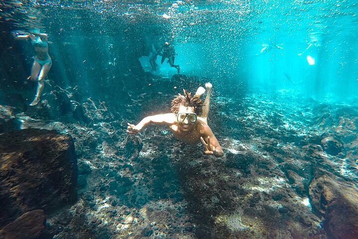 Swimmers enjoying the clear turquoise water channels of Chemka Hot Springs under green trees
