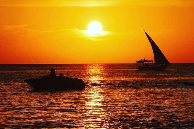 Traditional wooden dhow sailboats gliding smoothly across calm waters under a dramatic golden ocean sunset in Zanzibar